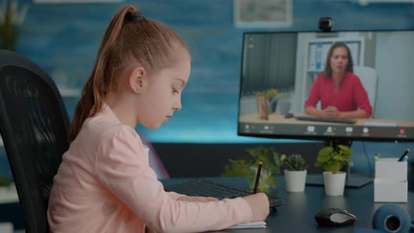 Pupil Writing on Textbook and Talking to Teacher on Video Call alt