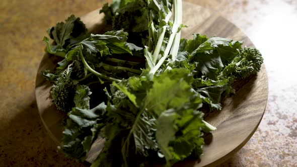 Clusters of stalks of fresh rapini on a round cutting board rotating in beautiful backlit light. alt