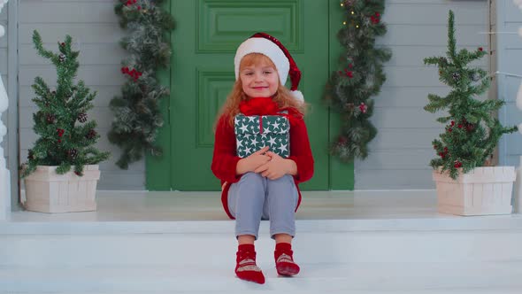 Joyful Smiling Toddler Child Girl Kid Sitting at Decorated House Porch Holding One Christmas Box alt
