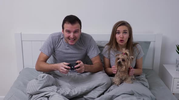 Happy Young Couple Lies in Bed with Small Dog alt