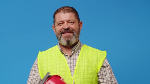 Smiling Senior Man Builder in Vest and Hardhat Against Blue Background