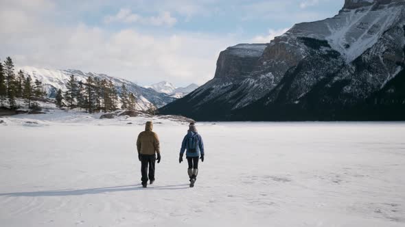 The Incredible Ice Lake in Rocky Mountains with Tourist Couple Hikers Walking Away to Beautiful Scen alt
