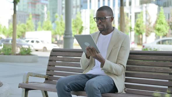 Upset African Man Reacting to Loss on Tablet While Sitting Outdoor on Bench alt