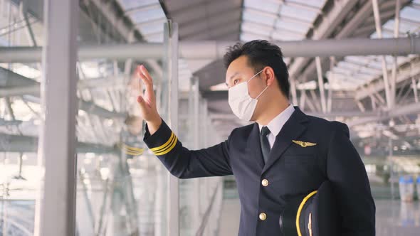 Airliner pilot wearing face mask walking in airport terminal and looking airplane with tired face. alt