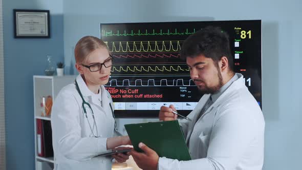 Female Doctor and Her Mixed Race Colleague Discussing EKG Data of the Athlete alt
