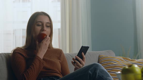 Pretty Girl Bites Red Apple and Looking at Something on Phone