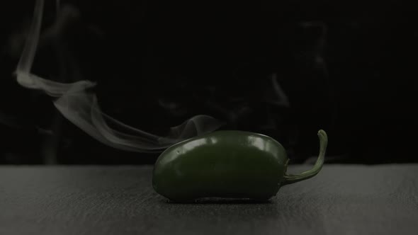 Green chili japaleno smoking on black background