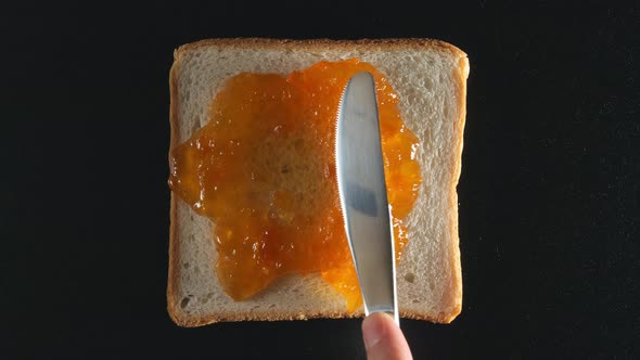 Human hand spreads an apricot jam on a bread