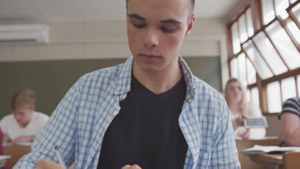 Caucasian boy writing in high school class alt