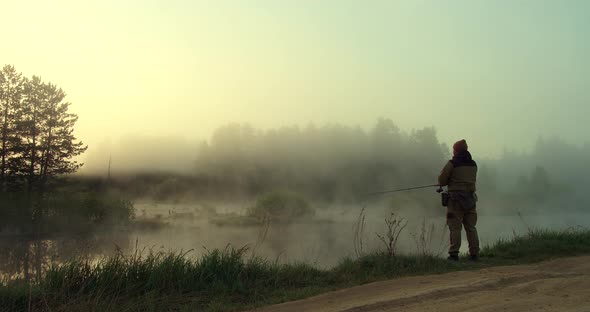 Unrecognizable Man Fishing in Lake at Dawn