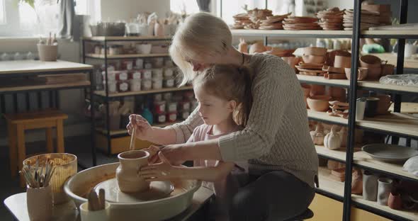 Grandmother Teaches Her Granddaughter Working on a Pottery Rotating Wheel