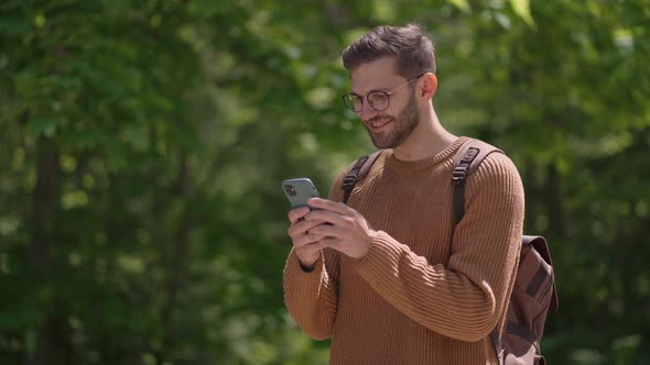 One Male Tourist with a Backpack with a Mobile Phone in a Forest Area Writes Messages Communicates alt