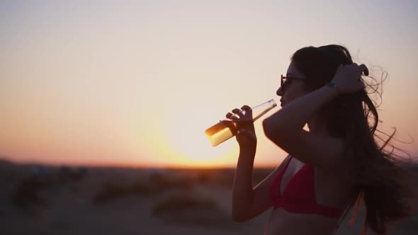 Beautiful Young Hipster Woman Drinking Beer and Enjoying Summer Sunset alt