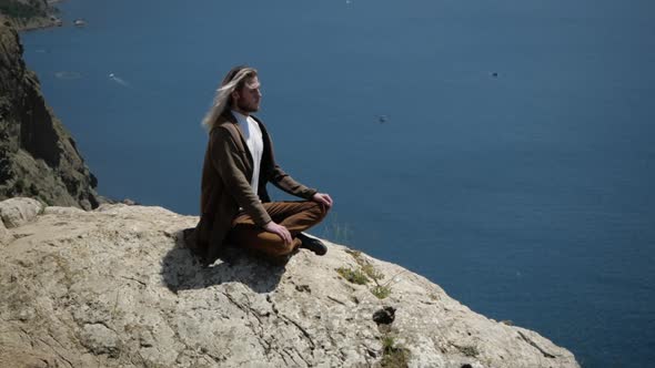 A Man Meditates on the Edge of a Cliff Enjoying the Rays of the Sun