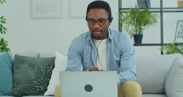 AfricanAmerican Businessman Sit on Sofa Talk with Client Solve Issues Distantly Through Headphones alt
