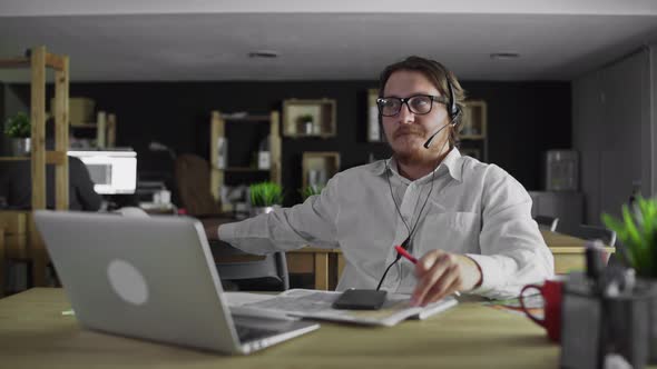 Young Manager in Headphones Is Working Looking in Smartphone in Office alt
