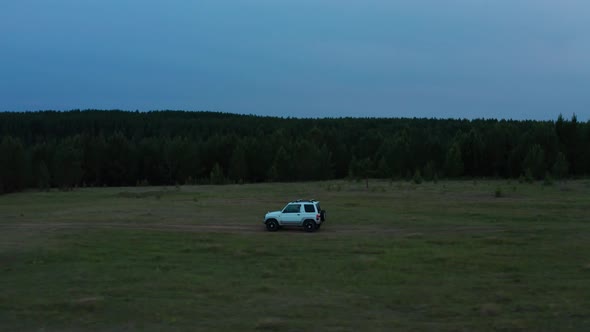 Aerial View of a Car Driving in Nature on a Field at Sunset alt