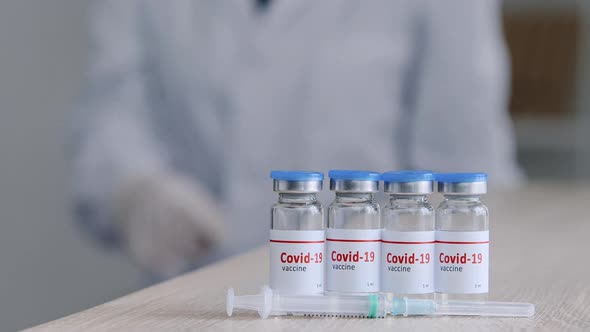 Closeup of Four Jars Bottles with Covid19 Vaccine Stand on Wooden Table in Clinic Near Syringe alt