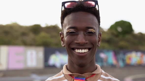 Young gay african man with make up smiling on camera at LGBT pride parade