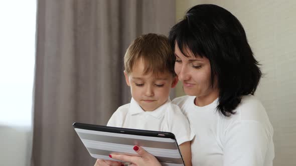 Mom and Her Child Spend Time at the Tablet at Home, Playing and Watching Cartoons, Playing Video alt