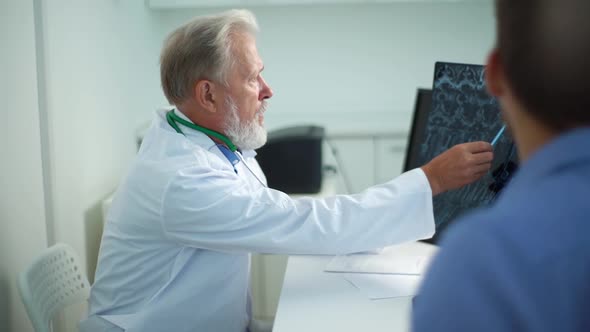 View From Back of Male Patient Listening Mature Adult Doctor with MRI Scan Giving Professional alt