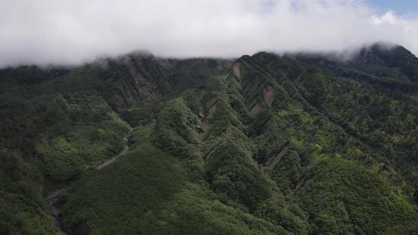 Aerial view of flying in a tropical forest, mountain, and valley in Indonesia. alt