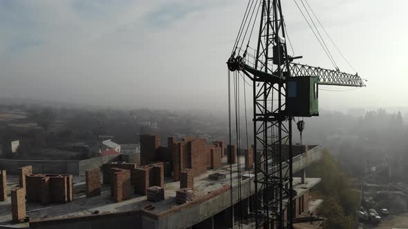 Birds eye view on tower crane in fog standing next to residential building. alt