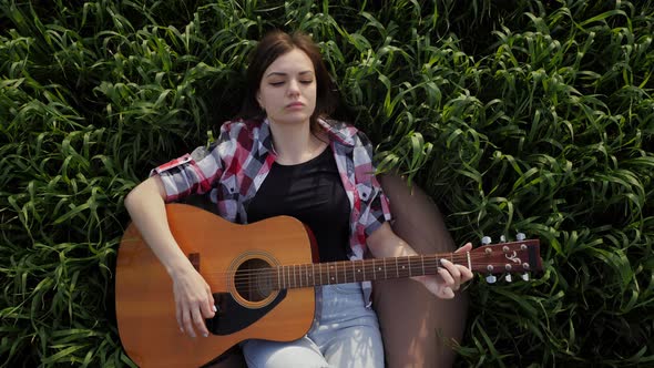 Woman Lies in a Wheat Field Plays Music on Guitar and Sings in Slow Motion at Sunset alt