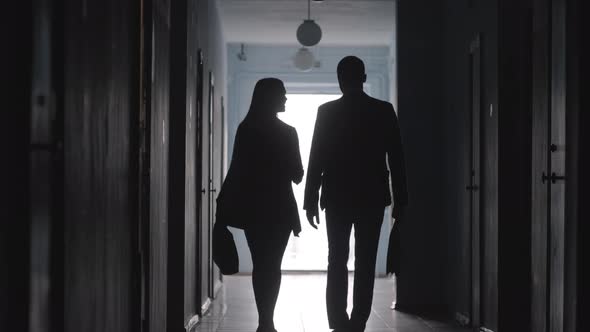 Silhouettes of Businessman and Businesswoman Walking through Hallway 