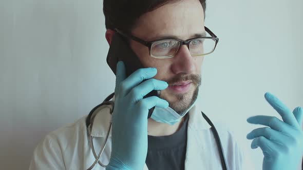 A Young Handsome Doctor Wearing Glasses and a Medical Face Mask Gives a Consultation Over the Phone.