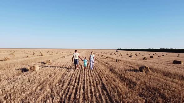 Happy Family with a Young Son Walks Through a Mown Wheat Field on a Sunny Summer Day Holding Hands