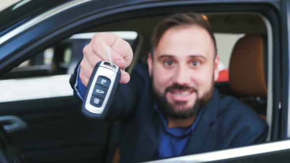 Blurred Positive Man Sitting in Driver's Seat of His New Car, Showing His New Car Keys and Smiling