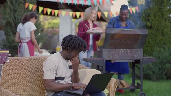 Absorbed African American Young Man Surfing Internet on Laptop with Group of Cheerful Friends alt