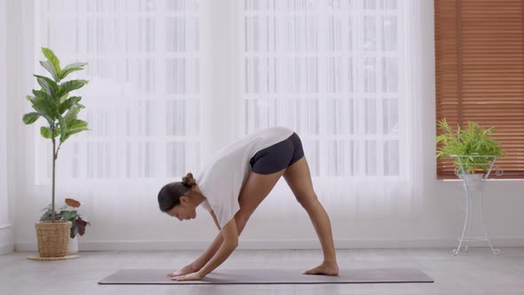 In the morning, an Asian woman is doing yoga, standing forward bend exercise alt