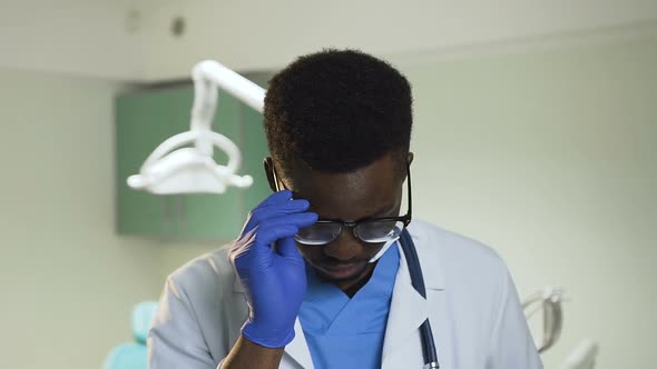 Young African Doctor Wearing Glasses in the Hospital Office. alt