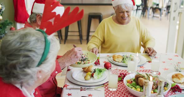 Group of happy caucasian senior friends in santa hats eating christmas dinner together at home alt