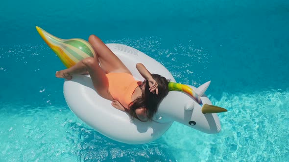 Woman Is Tanning on Rubber Ring Unicorn in Swimming Pool alt