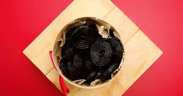 Rotation of Tasty black liquorice candies in present box on red background
