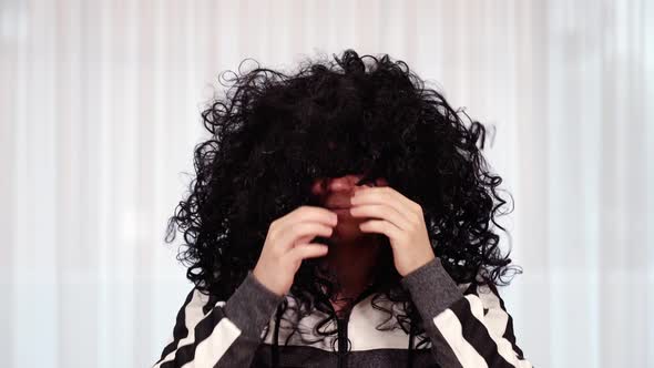 Guy Puts on Black Curly Hair Wig Under Bright Electric Light alt