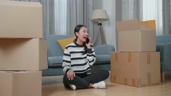 Asian Woman With Cardboard Boxes Talking On Smartphone After Moving Into A New House  alt