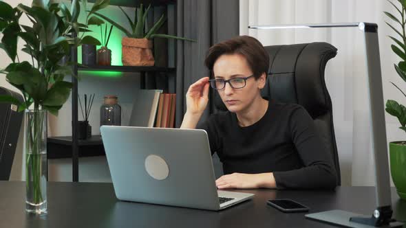 Overworked businesswoman is sitting at workplace desk and using laptop computer alt
