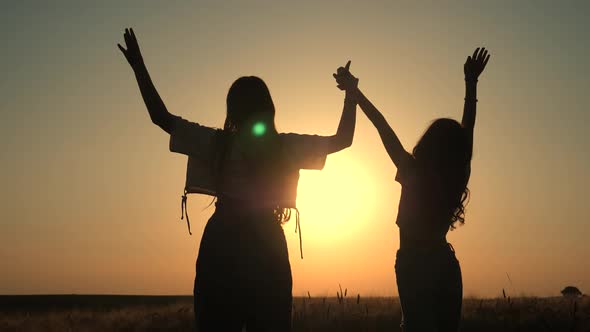 silhouette of a happy two girls and happy time sunset. Holding hands up