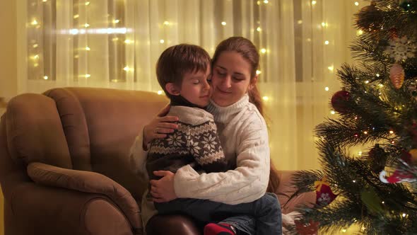 Cute Boy Hugging His Mother in Armchair Next to Christmas Tree alt