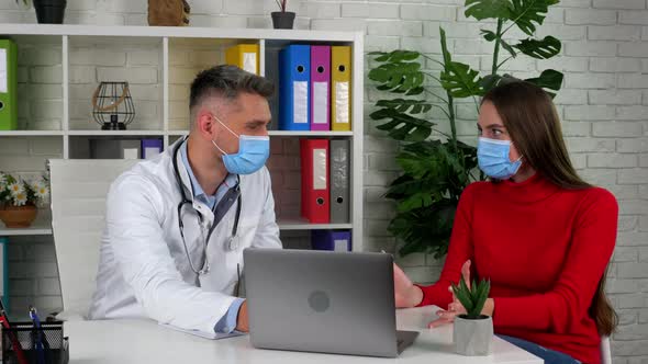 Doctor and patient wear protective masks on faces in hospital office talk listen alt