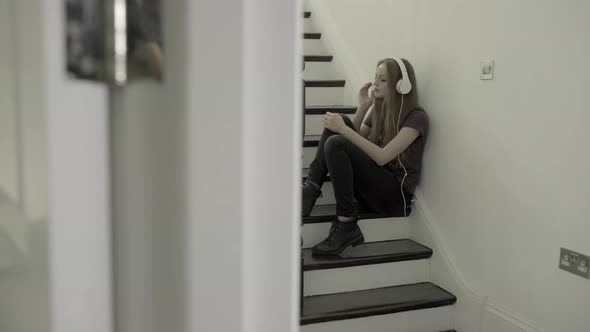 Teenager girl on staircase with smart phone and headphones