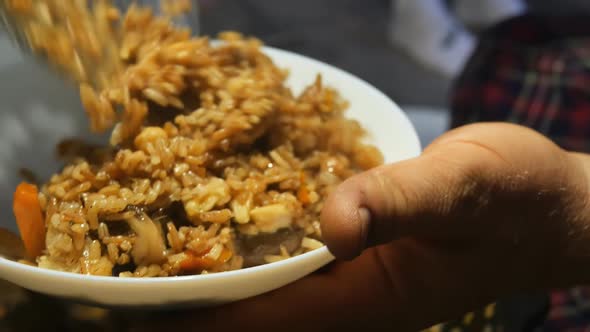 a Person Puts a Skimmer Into a White Bowl a Portion of Cooked Hot Uzbek Pilaf From Which Steam and alt