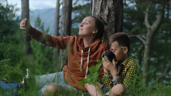 Mother with son making video call by phone while relaxing in the forest alt