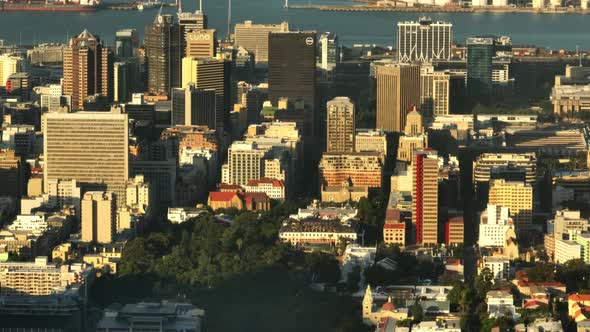 Elevated Footage of High Rise Buildings in City Centre Lit By Sun and Harbour in Background alt