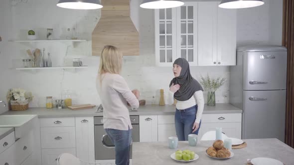 Adult Caucasian and Muslim Woman Arguing at Home, Lady in Hijab Turning Back To Friend. Two Friends alt