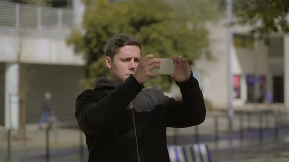 Serious Young Man Photographing with Smartphone on Street alt